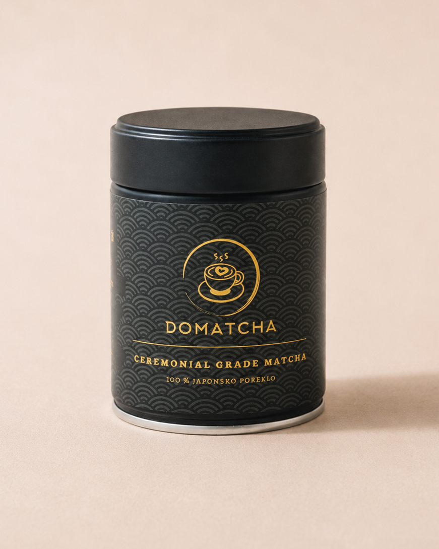 A black cylindrical metal canister of Domatcha ceremonial grade matcha, featuring a gold wave pattern and gold lettering, set against a solid beige background.
