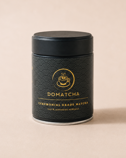 A black cylindrical metal canister of Domatcha ceremonial grade matcha, featuring a gold wave pattern and gold lettering, set against a solid beige background.